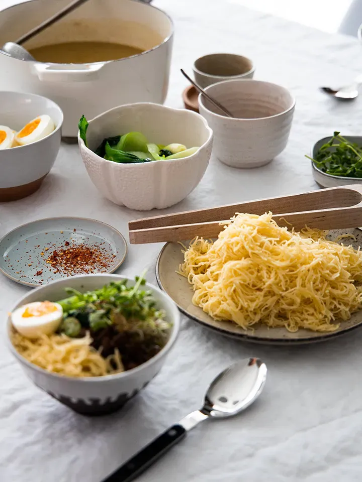 Ramen-Nudelsuppe mit knusprigem Faschiertem: Tisch mit Schalen voller Nudeln, Gemüse, Eiern und Gewürzen