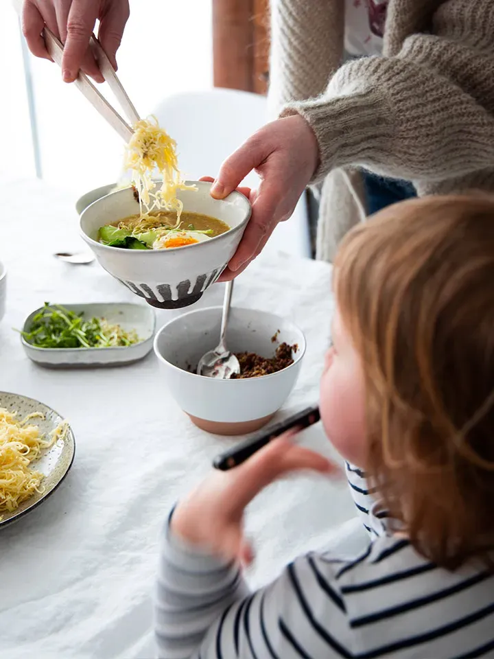 Person serviert einer sitzenden Person eine Schüssel Ramen-Nudelsuppe