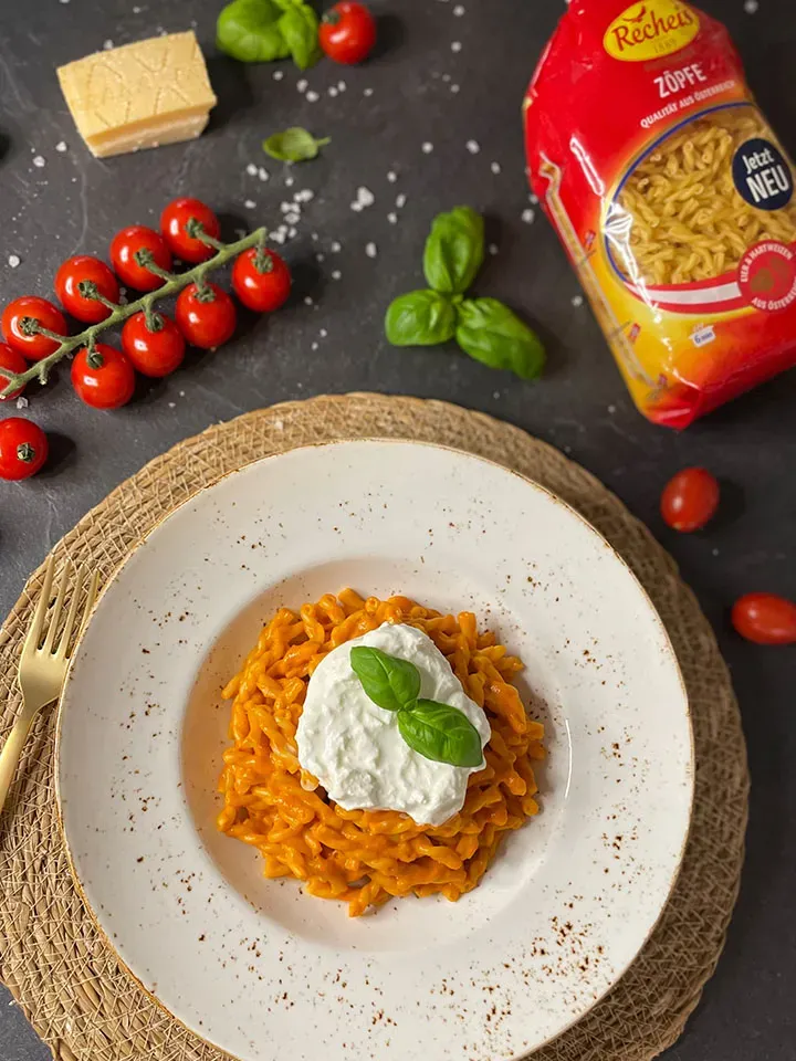 Cremige Pasta mit Datterini-Tomatensauce, Burrata und Basilikum, umgeben von Tomaten, Käse und Nudeln