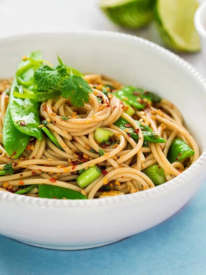 Sesamspaghetti mit Edamame und Frühlingszwiebel in einer Schüssel, mit Zuckerschoten und frischen Kräutern