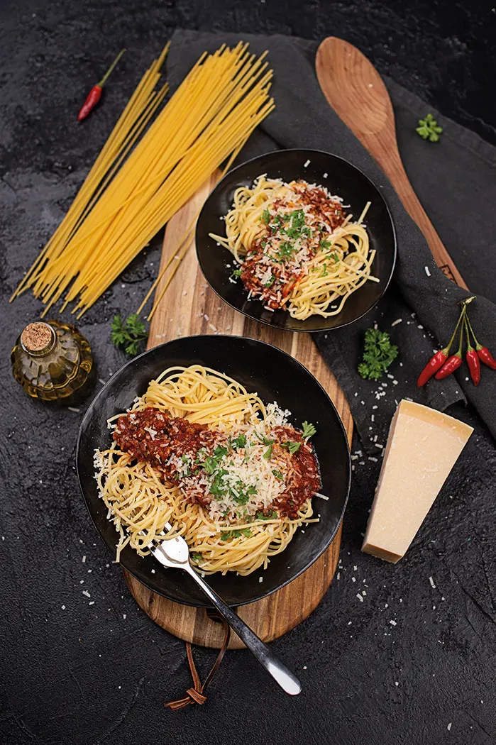 Spaghetti Blitzbolognese mit Parmesan auf zwei Tellern auf einem Holzbrett mit Zutaten