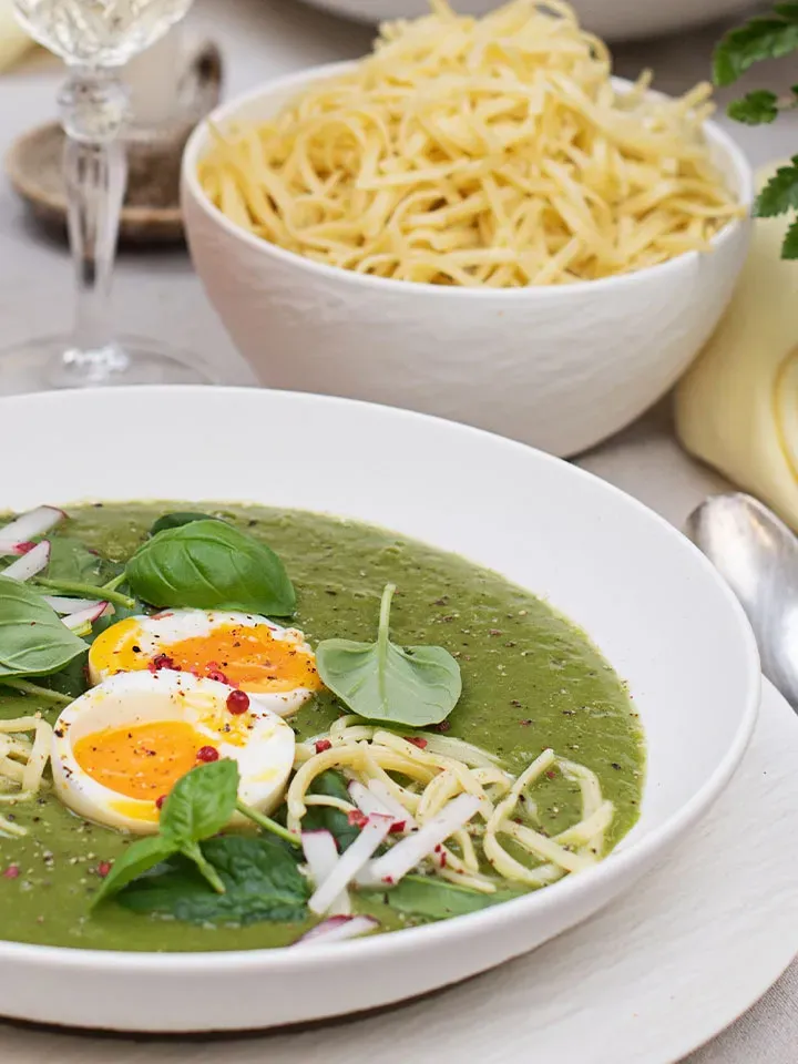 Grüne Spinatsuppe mit Ei, Nudeln und frischen Kräutern in weißer Schale