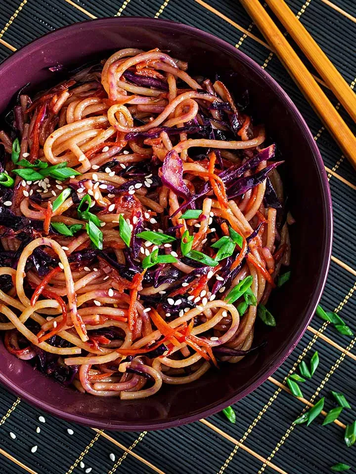Stir Fry mit Dinkelspaghetti, Rotkraut und Karotten in einer Schüssel mit Sesam und Frühlingszwiebeln auf Bambusmatte