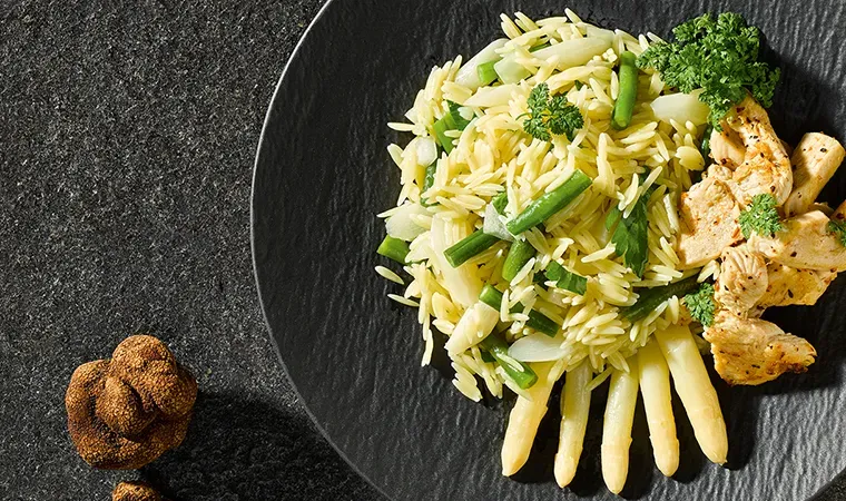Teigreis mit Fisolen, Spargel, Hühnerbrust und Sommertrüffel auf schwarzem Teller