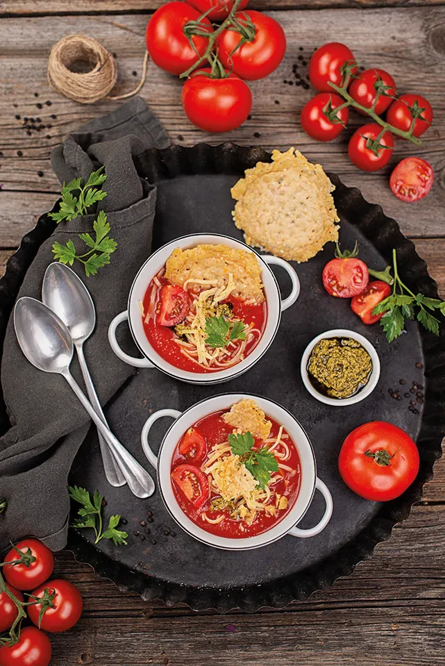 Tomaten-Nudelsuppe mit Parmesancrackern: zwei Schalen mit Käsechips und frischen Tomaten auf schwarzem Tablett