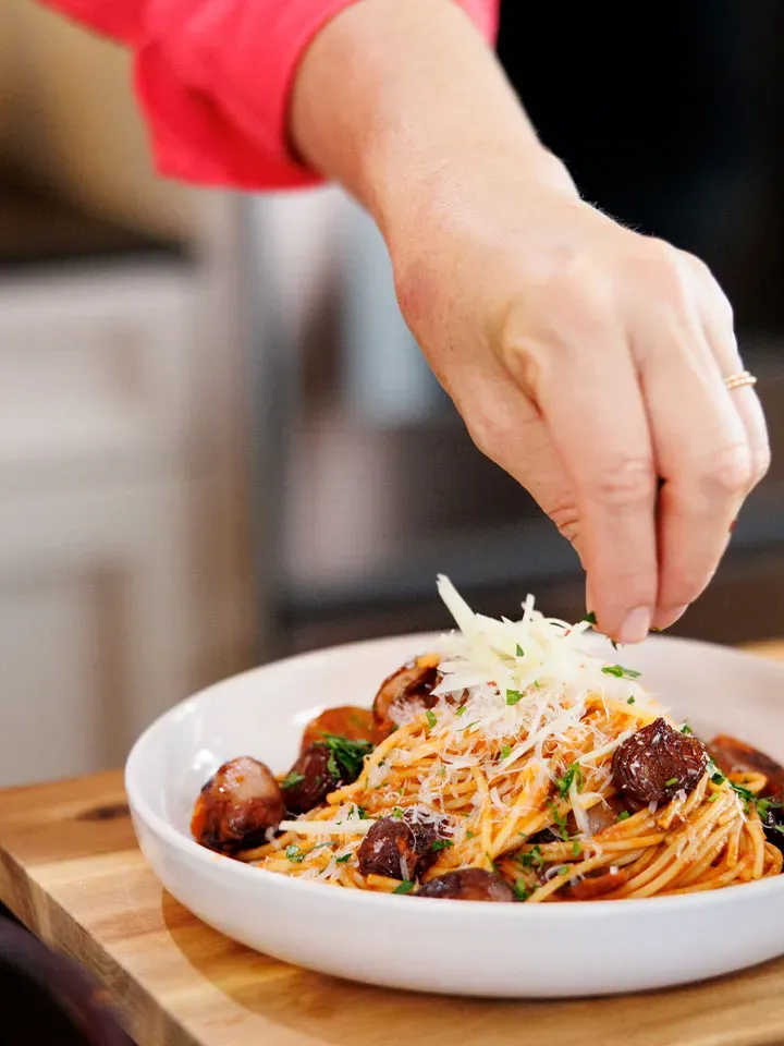Hand bestreut Spaghetti mit Tomatensauce und Ingwer mit Parmesan und Kräutern auf einem weißen Teller