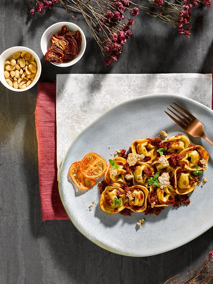 Tortelloni Spinat-Ricotta mit getrockneten Tomaten auf Tisch mit Deko und kleinen Schalen