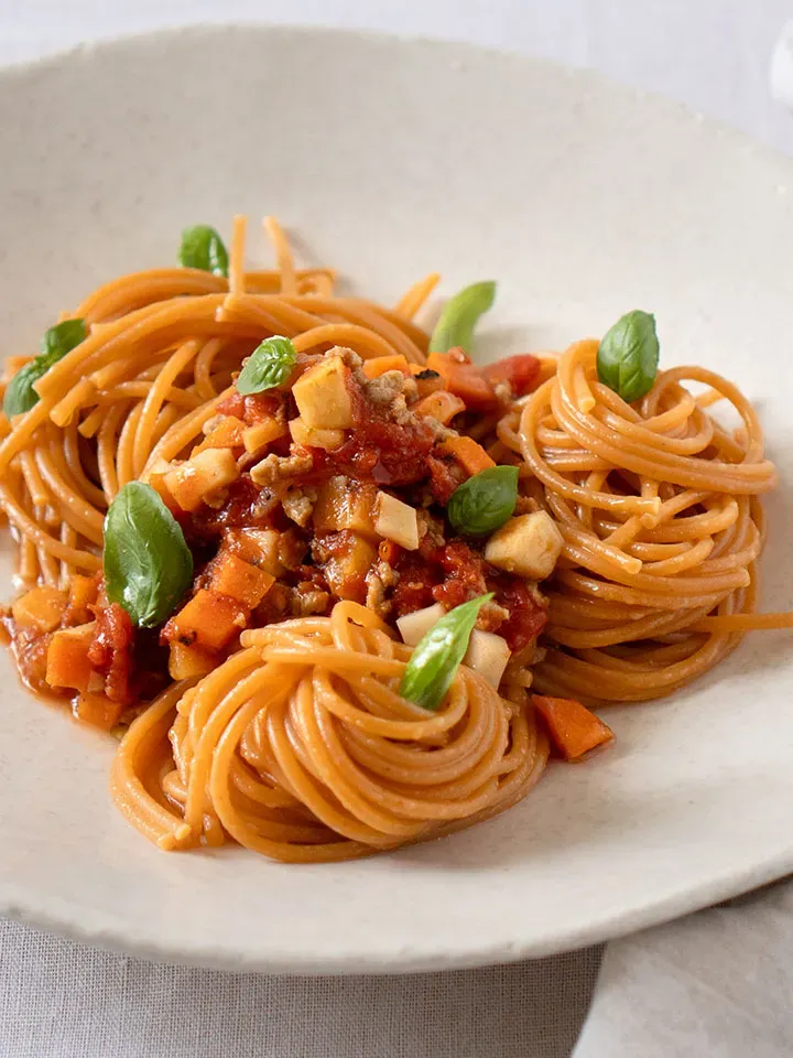 Vegane Spaghetti Bolognese mit Tomatensauce, Gemüsewürfeln und Basilikumblättern auf einem Teller