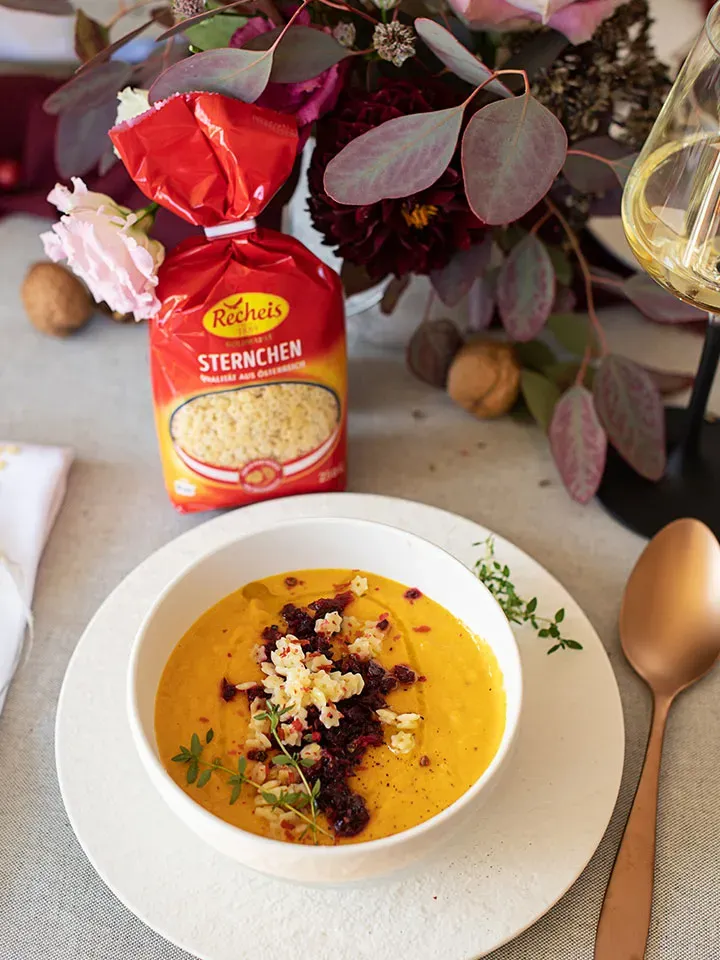 Weihnachtssuppe mit Sternchennudeln und Kräutern auf weißem Teller mit Löffel