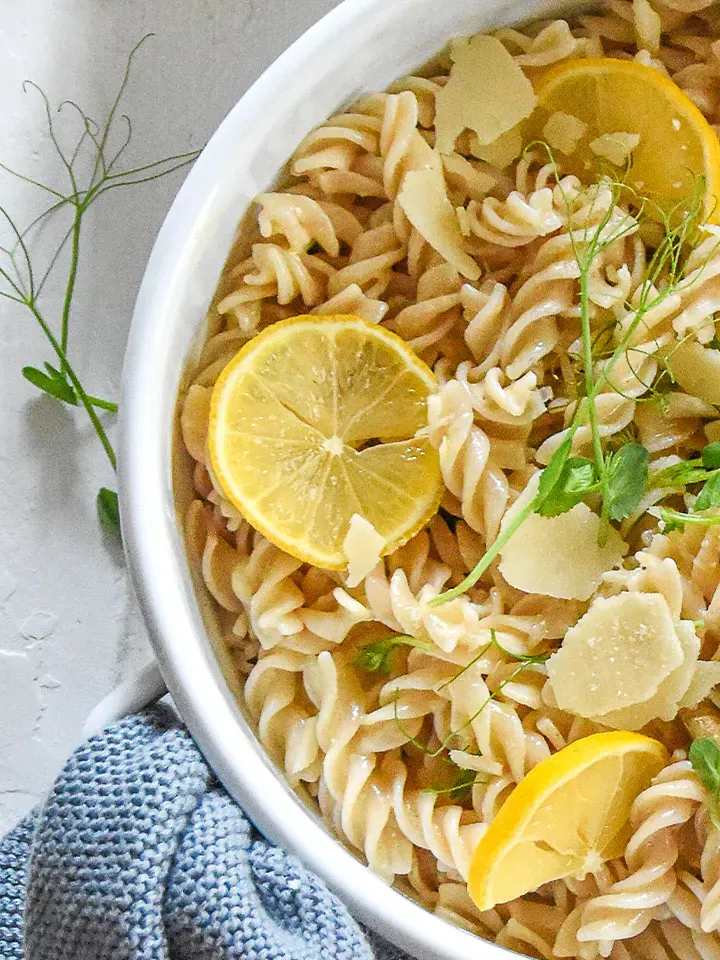 Nudeln mit Zitronensauce, Zitronenscheiben, Kräutern und Parmesan in weißer Schüssel