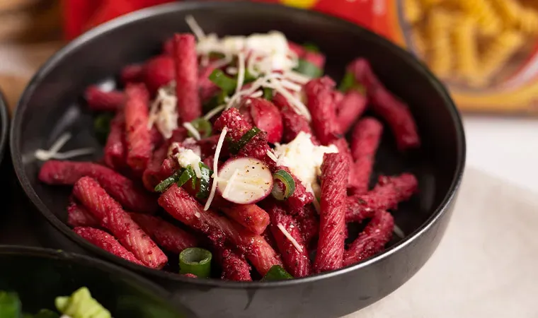 Rote-Bete-Pesto mit roter Pasta, Frühlingszwiebeln und Käse in einer schwarzen Schüssel