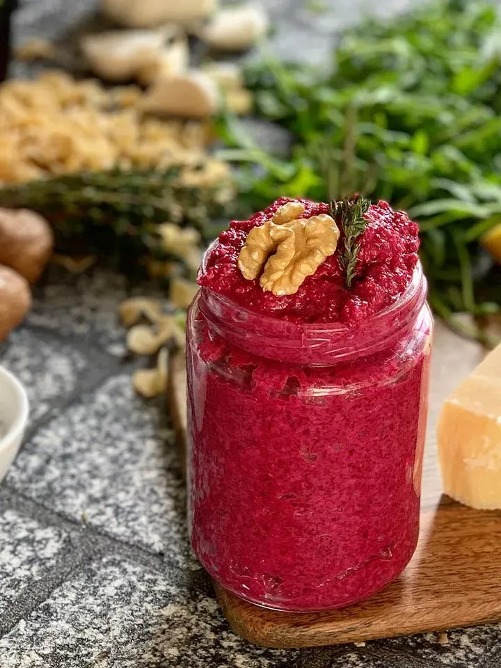Rote-Rüben-Pesto in einem Glas, mit Walnuss und Kräutern garniert, auf Holzbrett