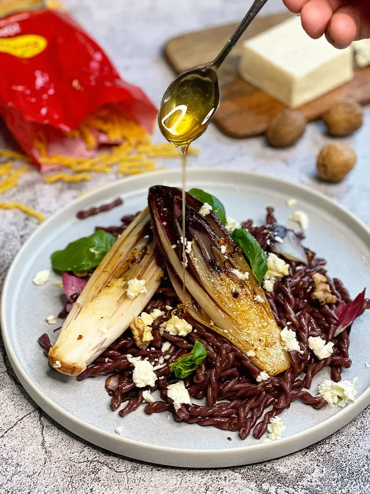 Honig wird über gegrillten Chicorée und Reis mit Feta für Rotweinnudeln (Drunken Pasta) auf einem Teller gegossen