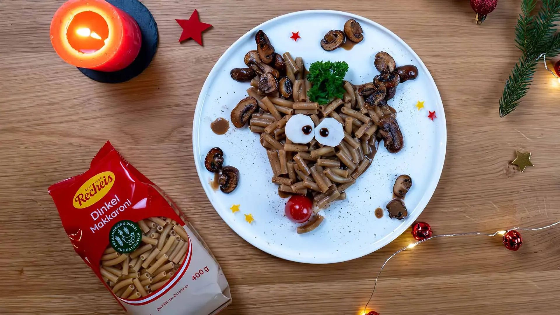 Rudolph, das Nudeltier: Pasta in Rentierform mit weihnachtlicher Dekoration auf Holztisch, dazu die Packung