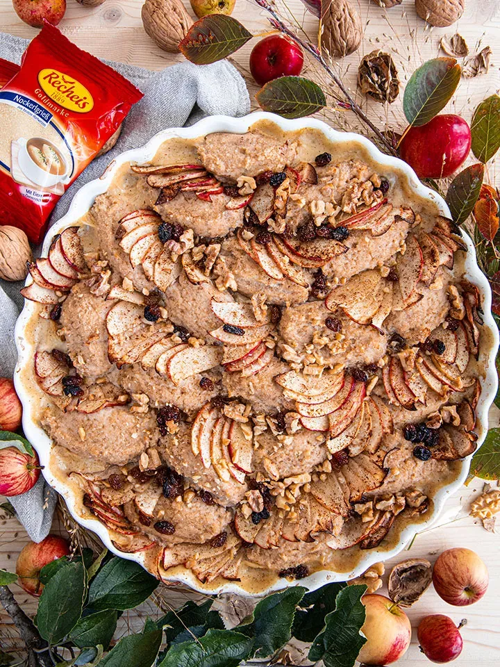 Scheiterhaufen mit Grießnockerl: Apfelauflauf mit Nüssen und Rosinen in einer weißen Form auf Holztisch