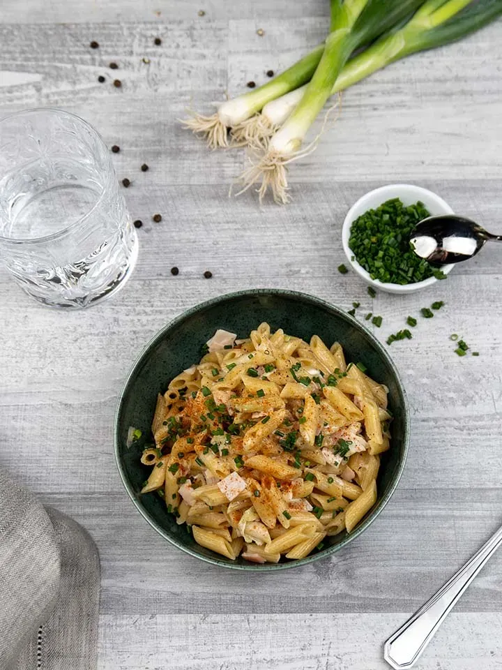 Schinken-Lauch-Penne mit Kräutern und Gewürzen in einer Schüssel auf hellem Holztisch