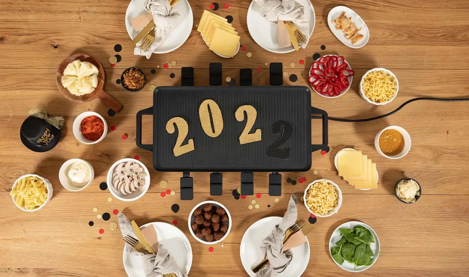 Silvester-Rezept mit Nudeln: Raclette-Grill mit Pfannkuchen in Form von 2022 und verschiedenen Zutaten auf Holztisch
