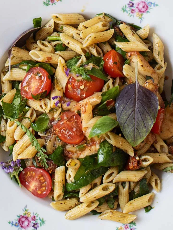 Nahaufnahme von Sommernudelsalat mit zarten Hühnerfilets: Penne mit Kirschtomaten und frischen Kräutern