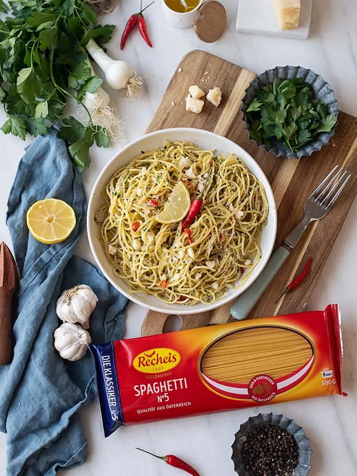 Spaghetti aglio e olio mit Kräutern, Knoblauch, Chili und Zitronenhälfte auf einem Teller auf Holzbrett