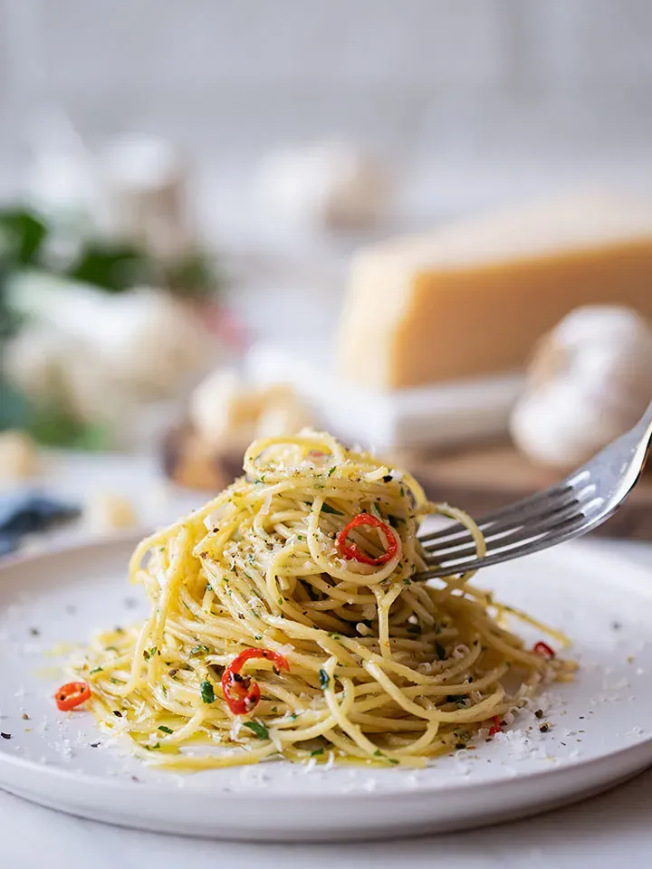Gabel mit Spaghetti aglio e olio und roten Chilischoten über einem weißen Teller