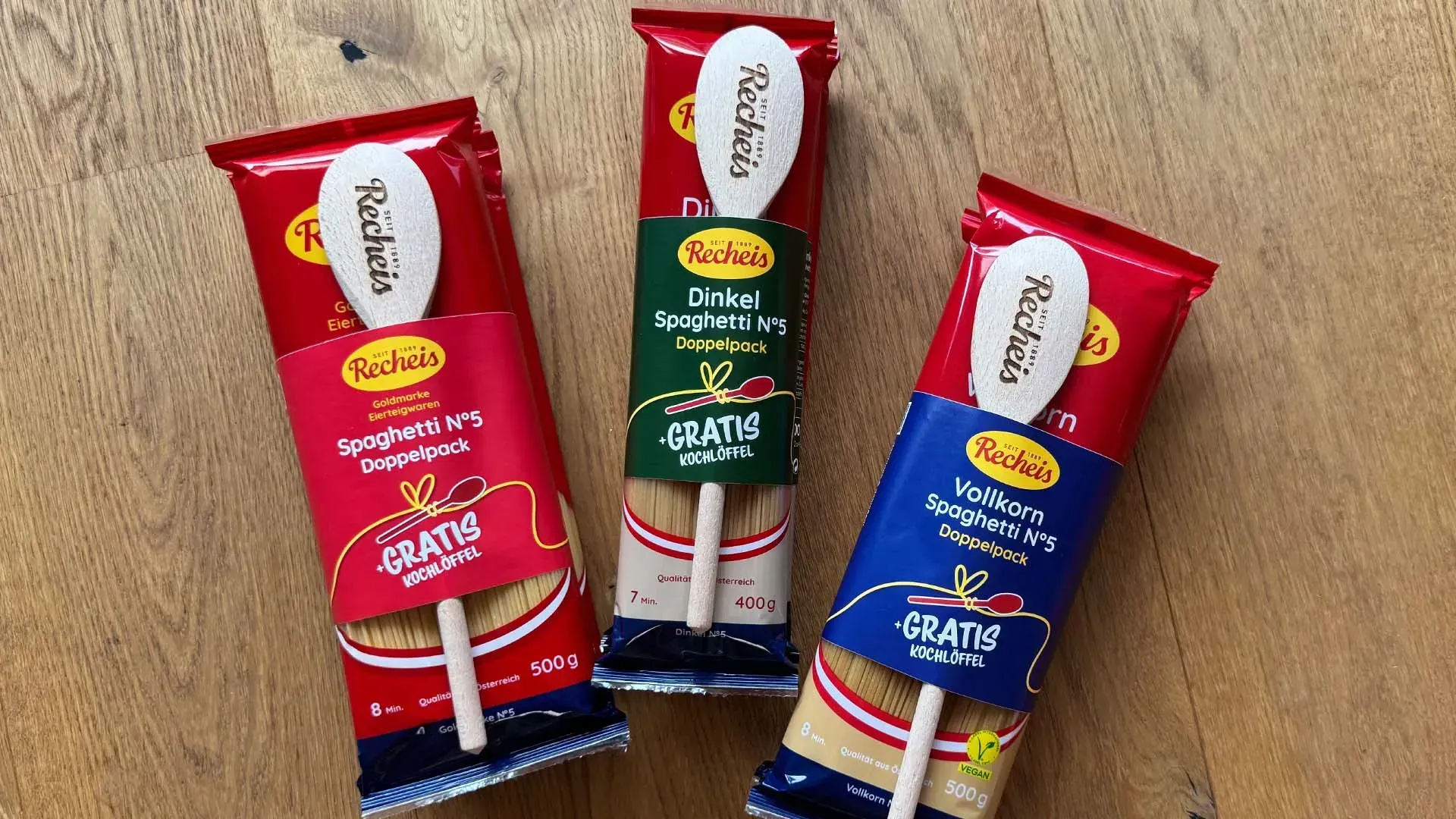 Drei Recheis Spaghetti-Doppelpacks – Goldmarke, Dinkel und Vollkorn – mit gratis Holzkochlöffel auf einem Holztisch