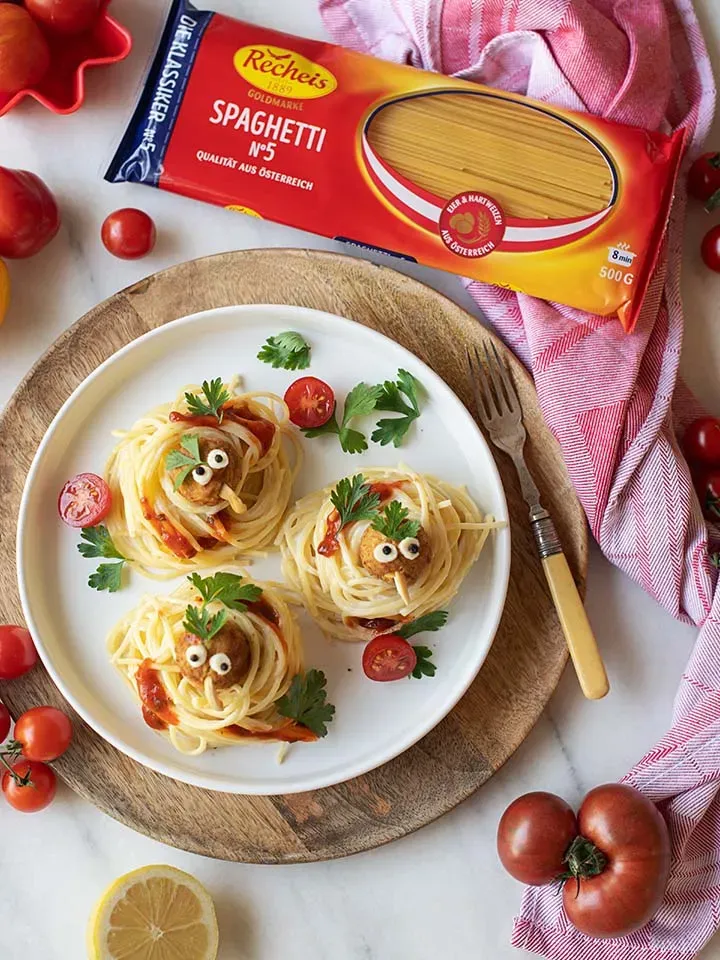 Spaghetti-Nester mit Gemüsebällchen als Vögel mit Gesichtern dekoriert, auf drei Tellern