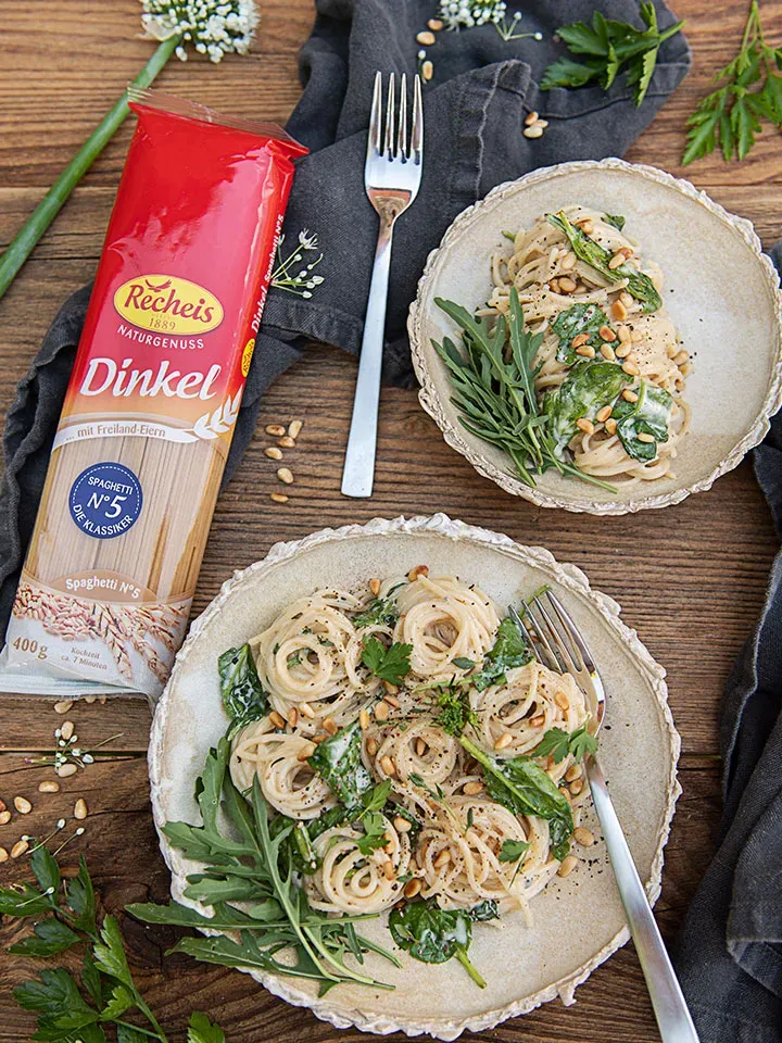 Spaghetti mit Gorgonzolasauce und grünem Salat auf zwei Tellern neben einer Packung Dinkel-Spaghetti