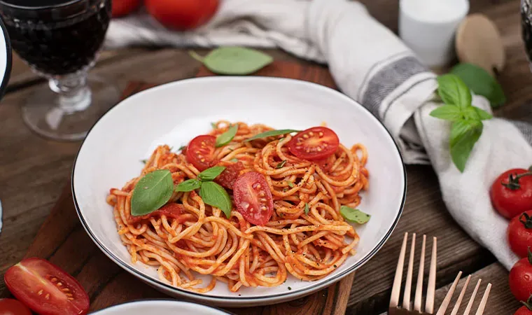 Vegane Spaghetti mit Tomatensauce, mit Basilikum und Tomaten garniert, auf einem Teller