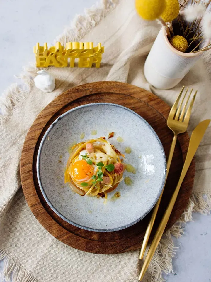 Spaghetti-Muffins für Ostern mit Spiegelei und Speck auf einem grauen Teller mit goldenem Besteck