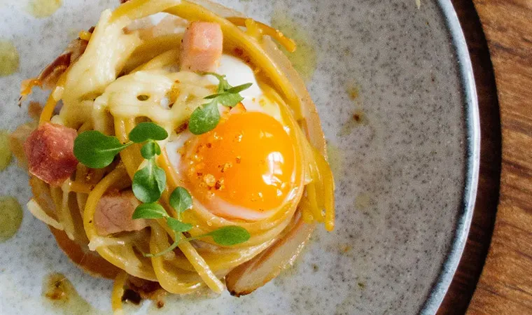 Pikante Spaghetti-Muffins mit Schinken, Spiegelei, Speck und Kräutern auf einem Teller