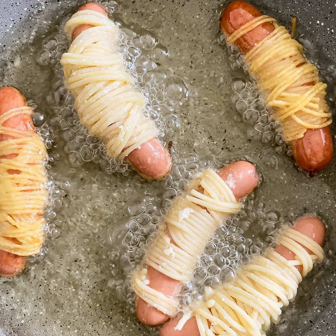 Spaghetti-Mumien braten: mit Spaghetti umwickelte Würstchen werden in Öl frittiert