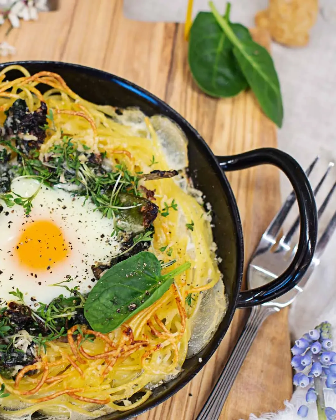 Spaghettinester mit Spiegelei, Kräutern und Spinat auf knusprigen Kartoffelspiralen in einer Pfanne