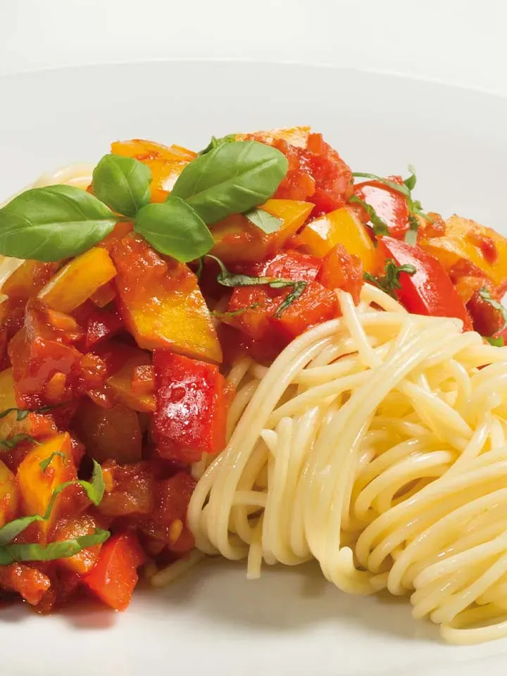 Spaghetti Pasta di Peppino mit Paprika-Tomaten-Sauce und frischem Basilikum auf weißem Teller