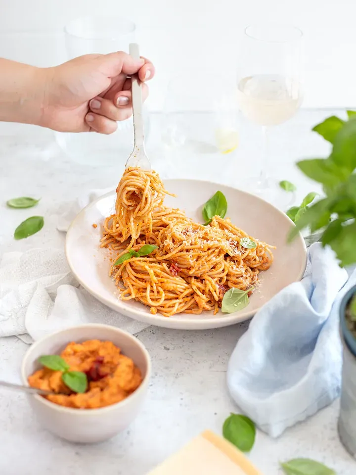 Hand dreht Spaghetti mit Pesto rosso und Basilikum auf einer Gabel