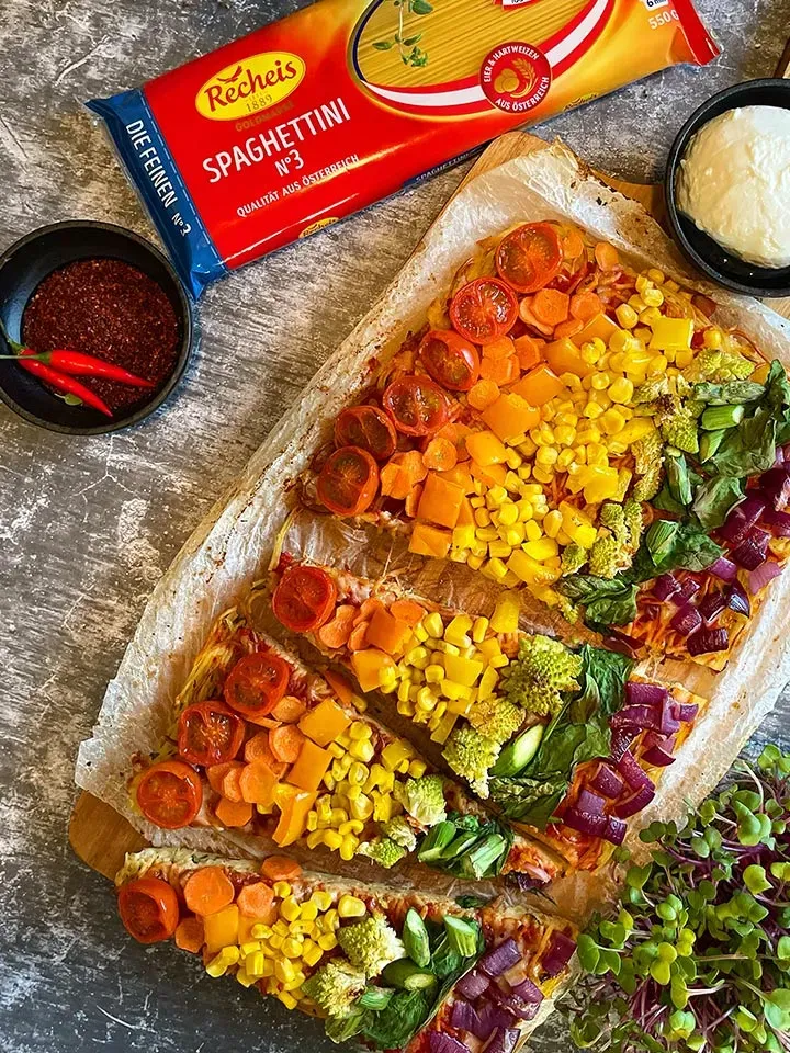 Spaghetti Pie mit buntem Gemüse, daneben eine Spaghetti-Packung und Schalen mit Gewürzen und Dip