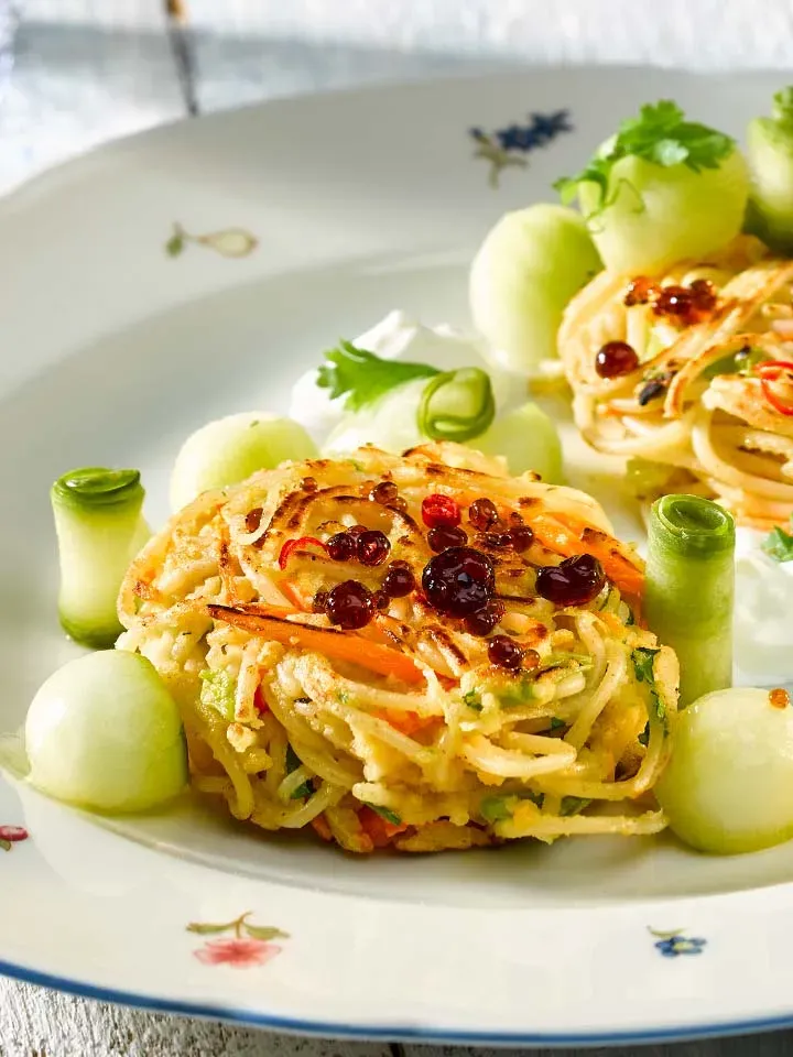 Spaghettipuffer mit Gurke, kleine gebratene Nudelkuchen mit Melonen- und Gurkenstücken auf einem Teller