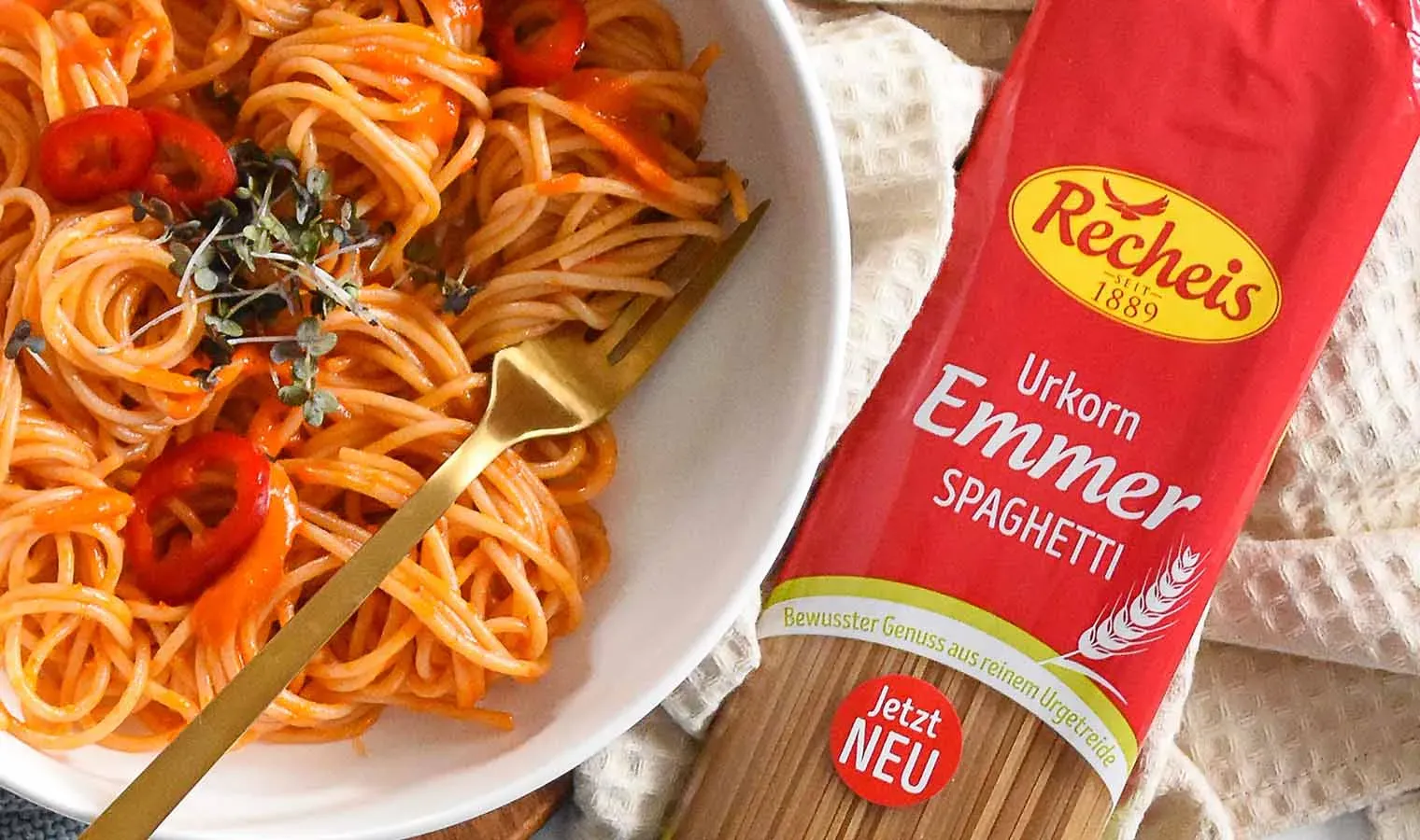Spaghetti mit Paprika in Tomatensauce auf einem Teller, daneben eine Packung Recheis Urkorn Emmer Spaghetti
