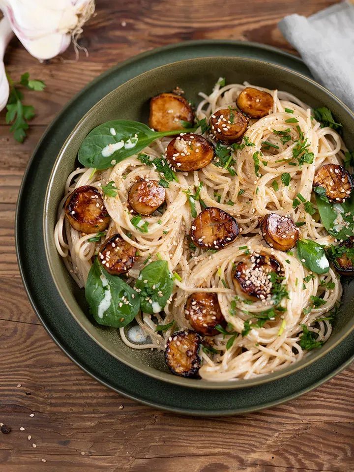 Spaghetti mit gebratenen Pilzen, Spinat und Sesam auf einem Teller auf Holztisch