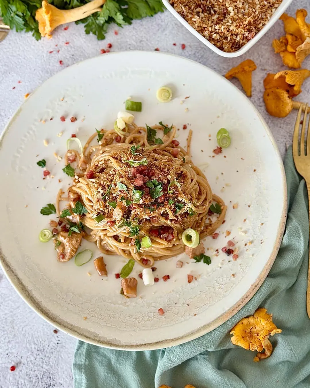Spaghetti mit Eierschwammerln und Misopaste, mit Kräutern dekoriert, auf grauem Untergrund