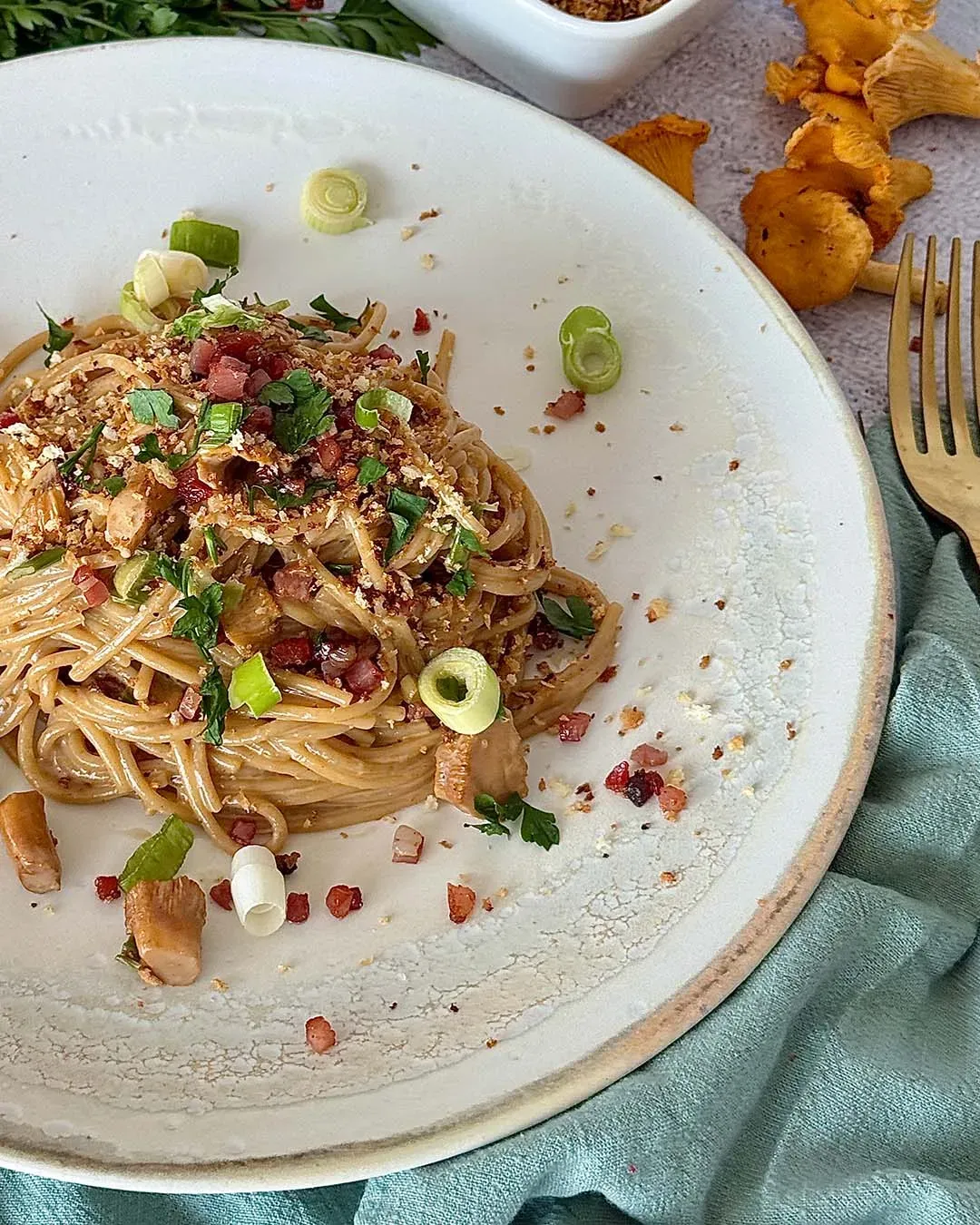 Spaghetti mit Eierschwammerln, Speckcrunch, Frühlingszwiebeln und Kräutern auf einem Teller