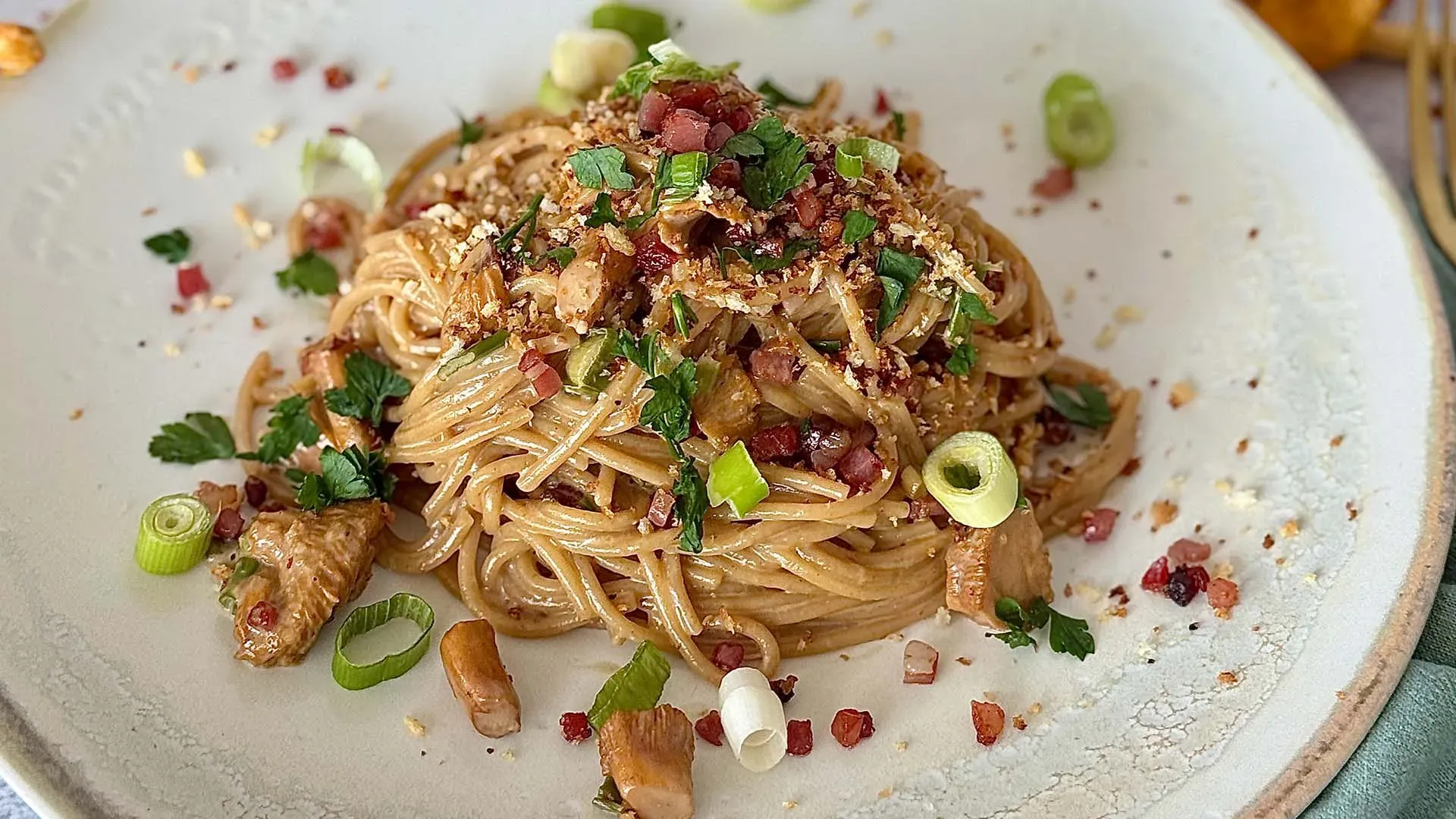 Spaghetti mit Eierschwammerlgulasch, Speck und Kräutern auf weißem Teller angerichtet