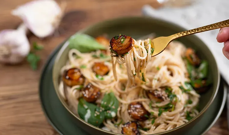Gabel mit Spaghettini und gebratenen Pilzen über einem Teller, vegane Jakobsmuscheln mit Weißweinsauce