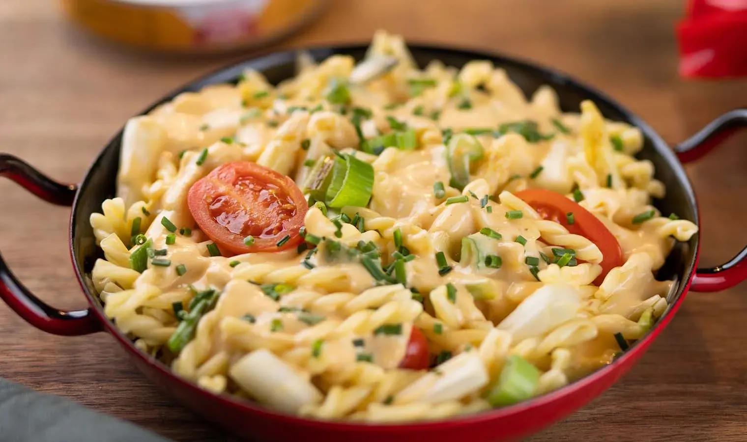Spargel-Nudelpfanne mit Käse, Tomaten und Frühlingszwiebeln in roter Pfanne