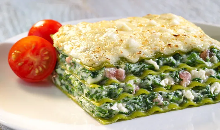 Stück Spinat-Feta-Lasagne mit Tomaten auf einem weißen Teller