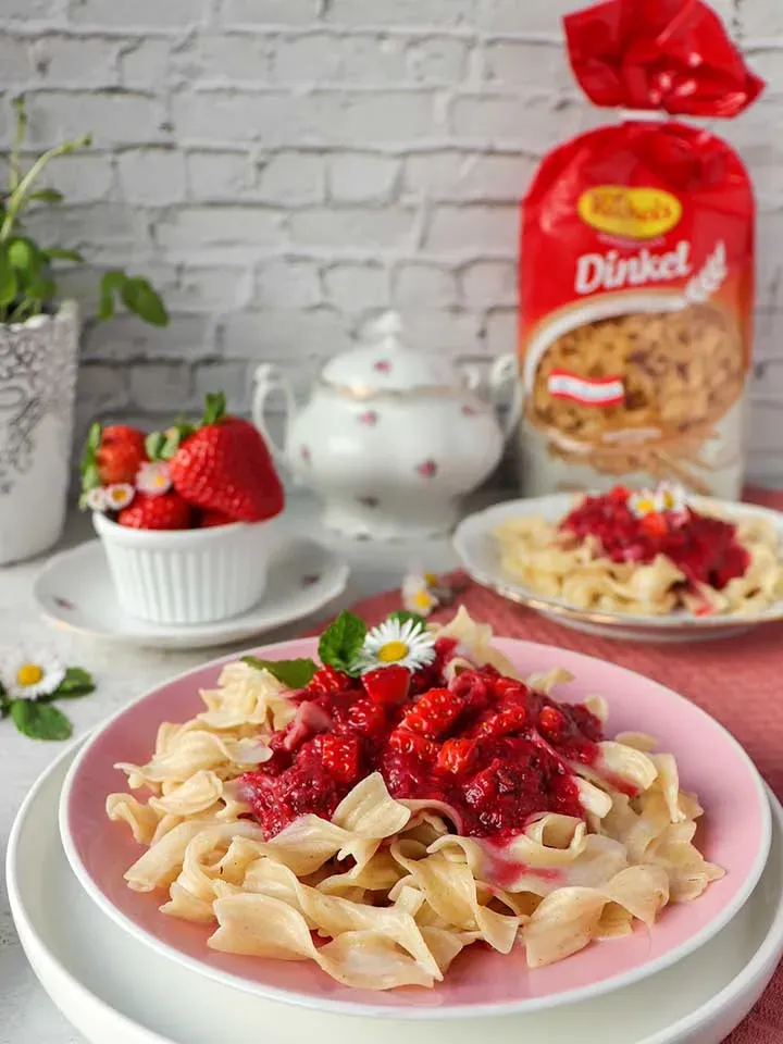 Süße Milchnudeln mit roter Erdbeersoße, mit Blüten und Minze dekoriert, auf einem Teller
