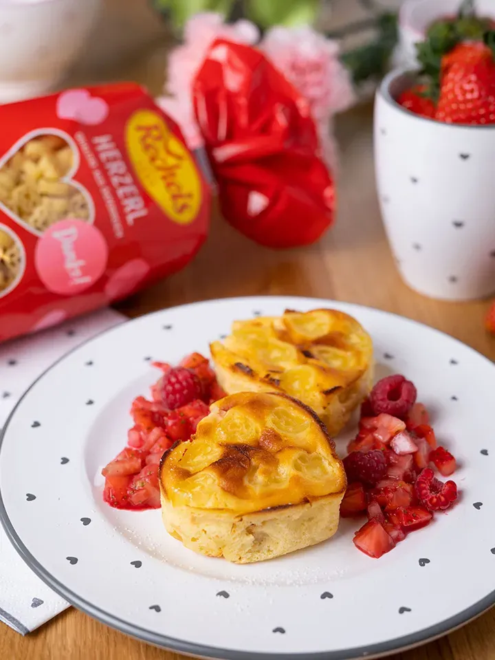 Süßer Nudelauflauf in Herzform mit Beeren auf einem weißen Teller mit Herzmuster