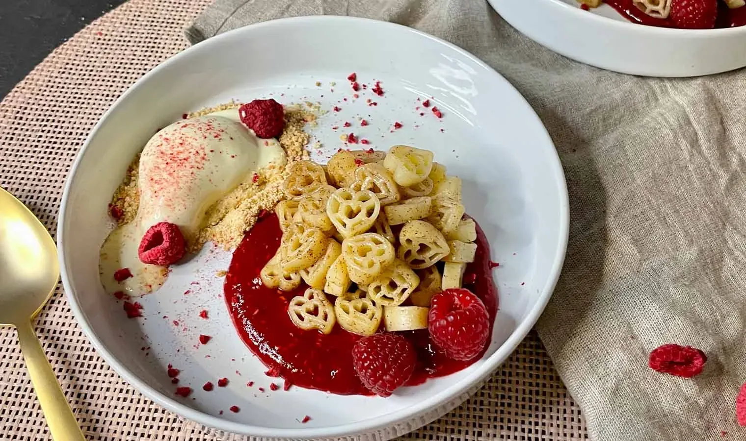 Süßes Nudelrezept mit Herznudeln, Himbeersauce, Sahne und Eis auf weißem Teller