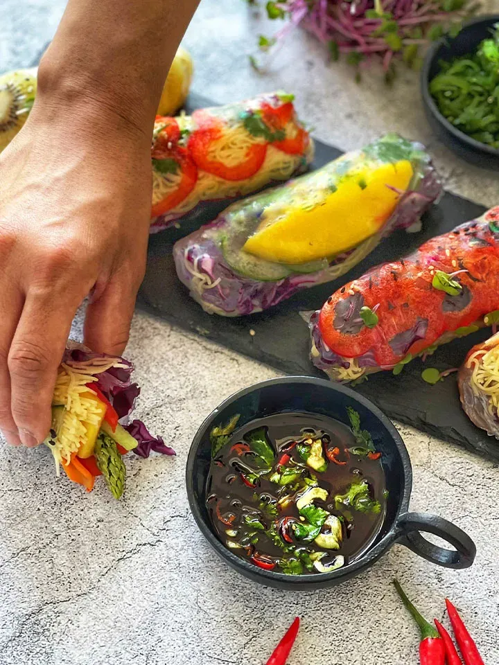 Hand nimmt eine Sommerrolle mit Gemüse und Kürbiskernöl-Dip