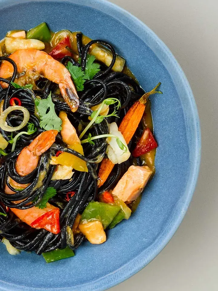 Sweet-and-Spicy-Pastabowl mit Fischcurry: schwarze Pasta mit Garnelen, Gemüse und Kräutern in blauer Schale