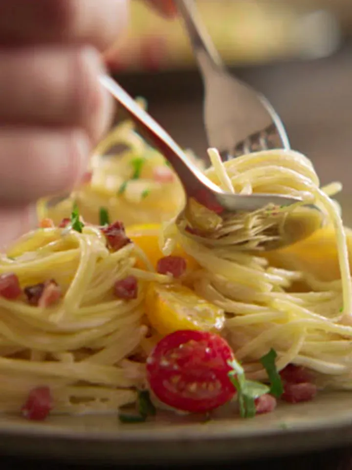 Nahaufnahme: Tiroler Spaghetti Carbonara mit Tomaten und Kräutern auf einem Teller